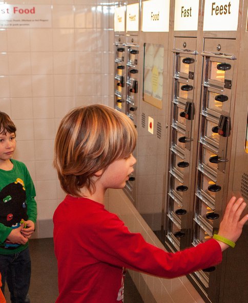 Afbeeldingen van kinderen op de tentoonstelling Feest! Weet wat je viert die bij een fastfoodmuur staan